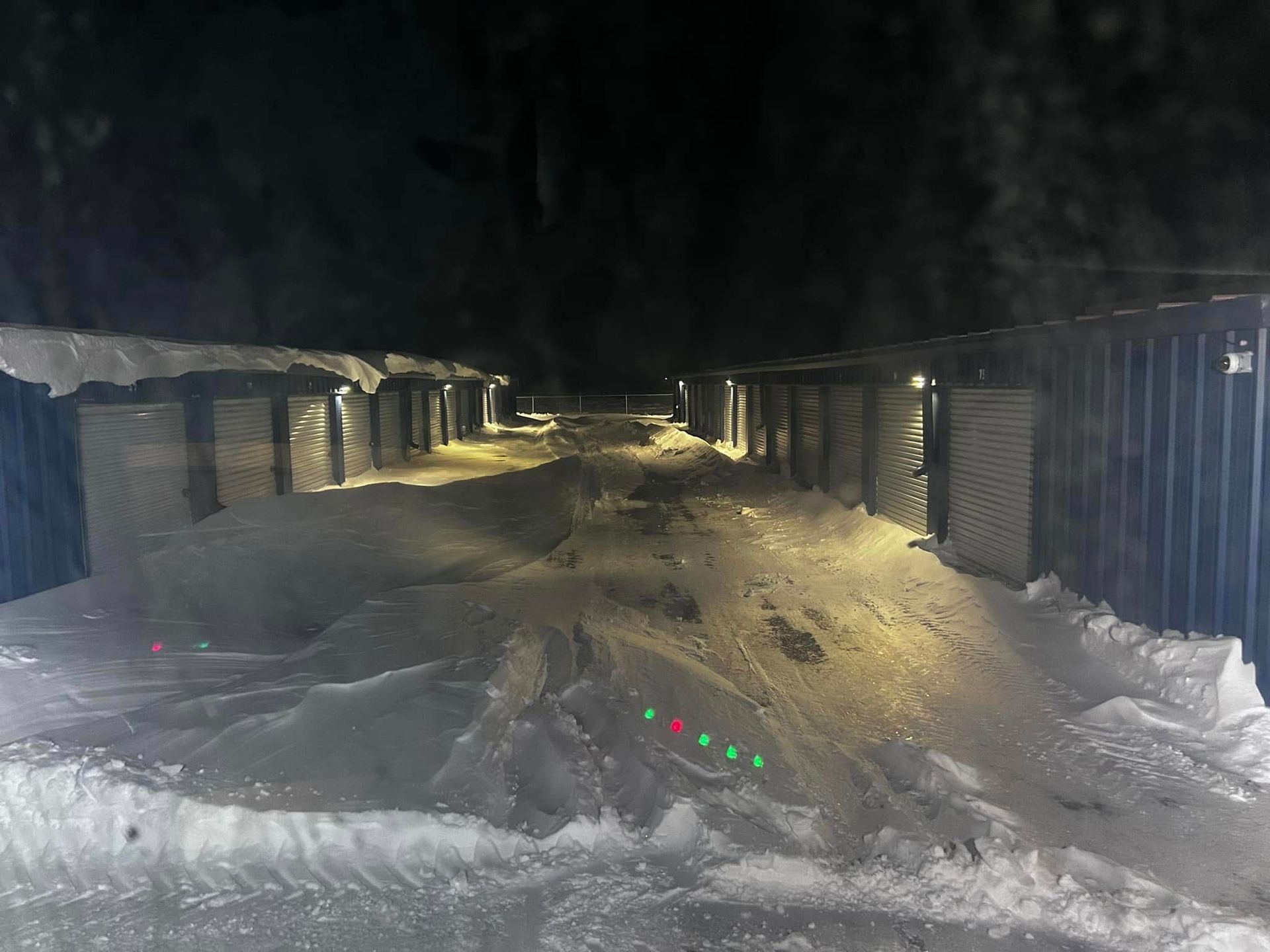 Snow-covered outdoor storage units at night with green/red lights on the ground.