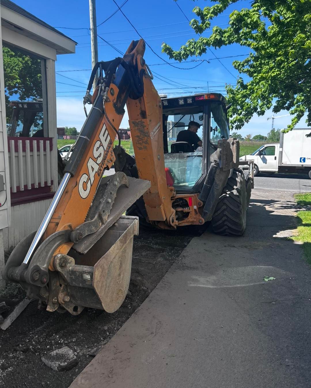A Case backhoe parked on a sidewalk next to a building. A person sits in the cab.