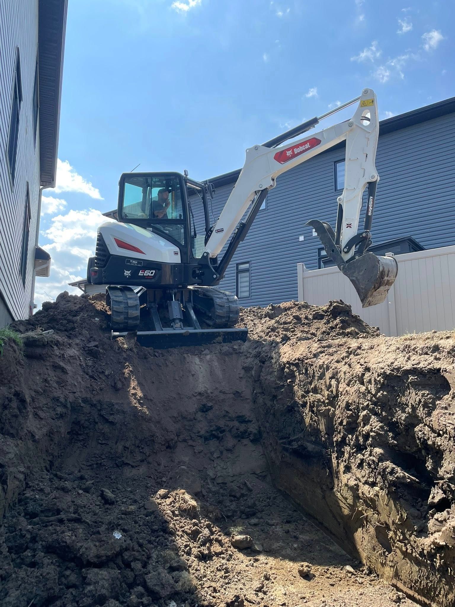 Excavator digging a trench next to a building under a blue sky.