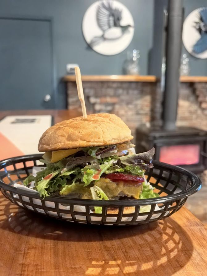 A burger in a black basket, on a wooden table, in a restaurant.