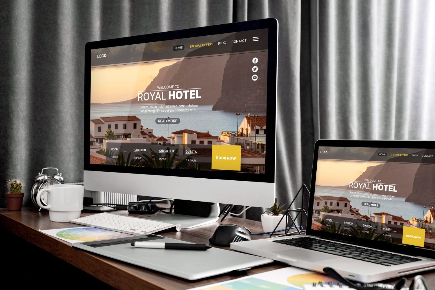 Desk with desktop and laptop showing a hotel website in a modern office setting