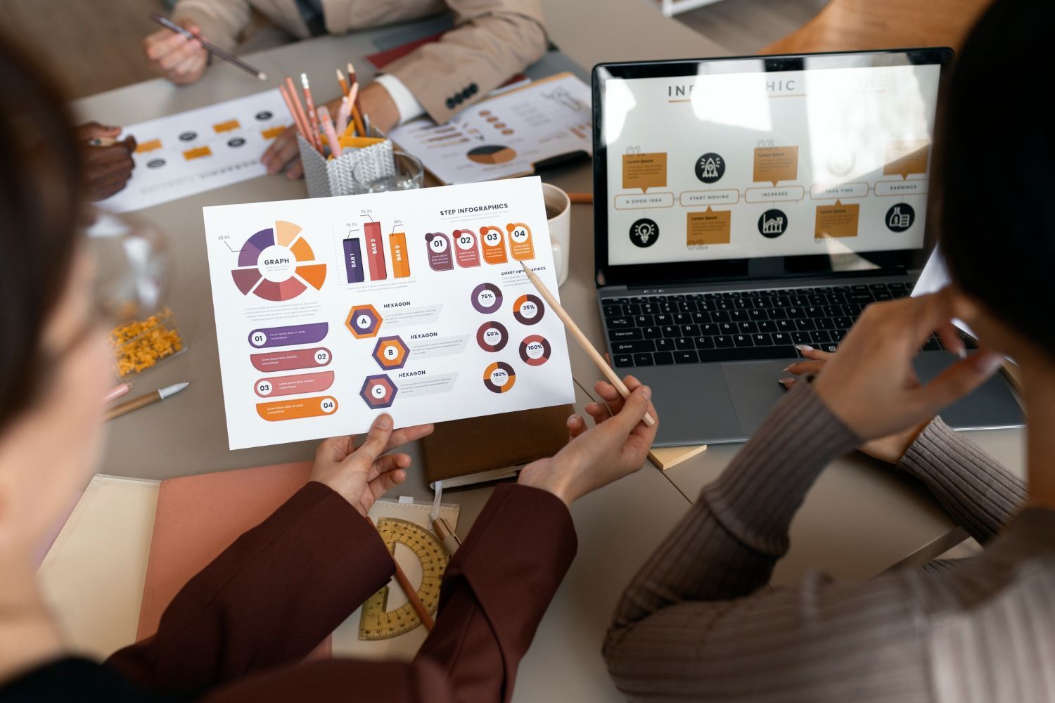 People reviewing colorful charts and graphs on a tablet and laptop at a meeting table