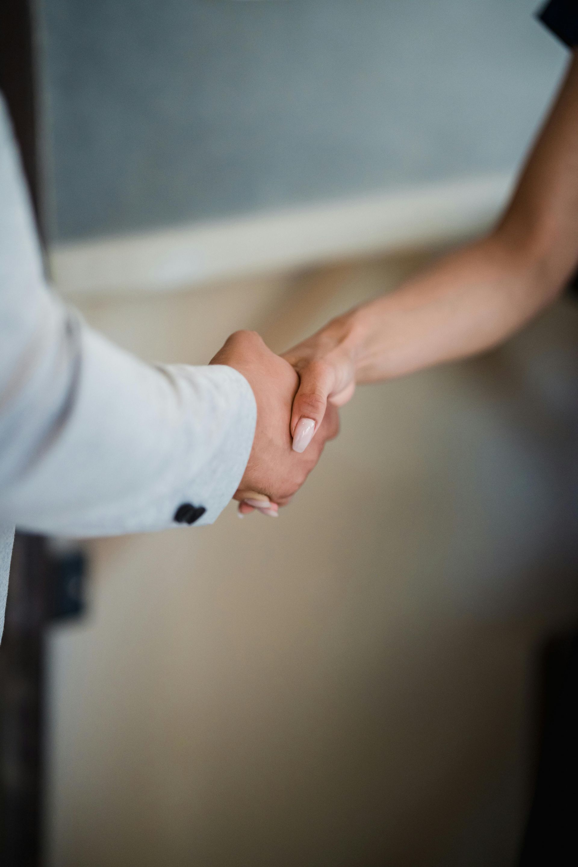 Two people shaking hands in a hallway, one in a light shirt and one in a dark top.