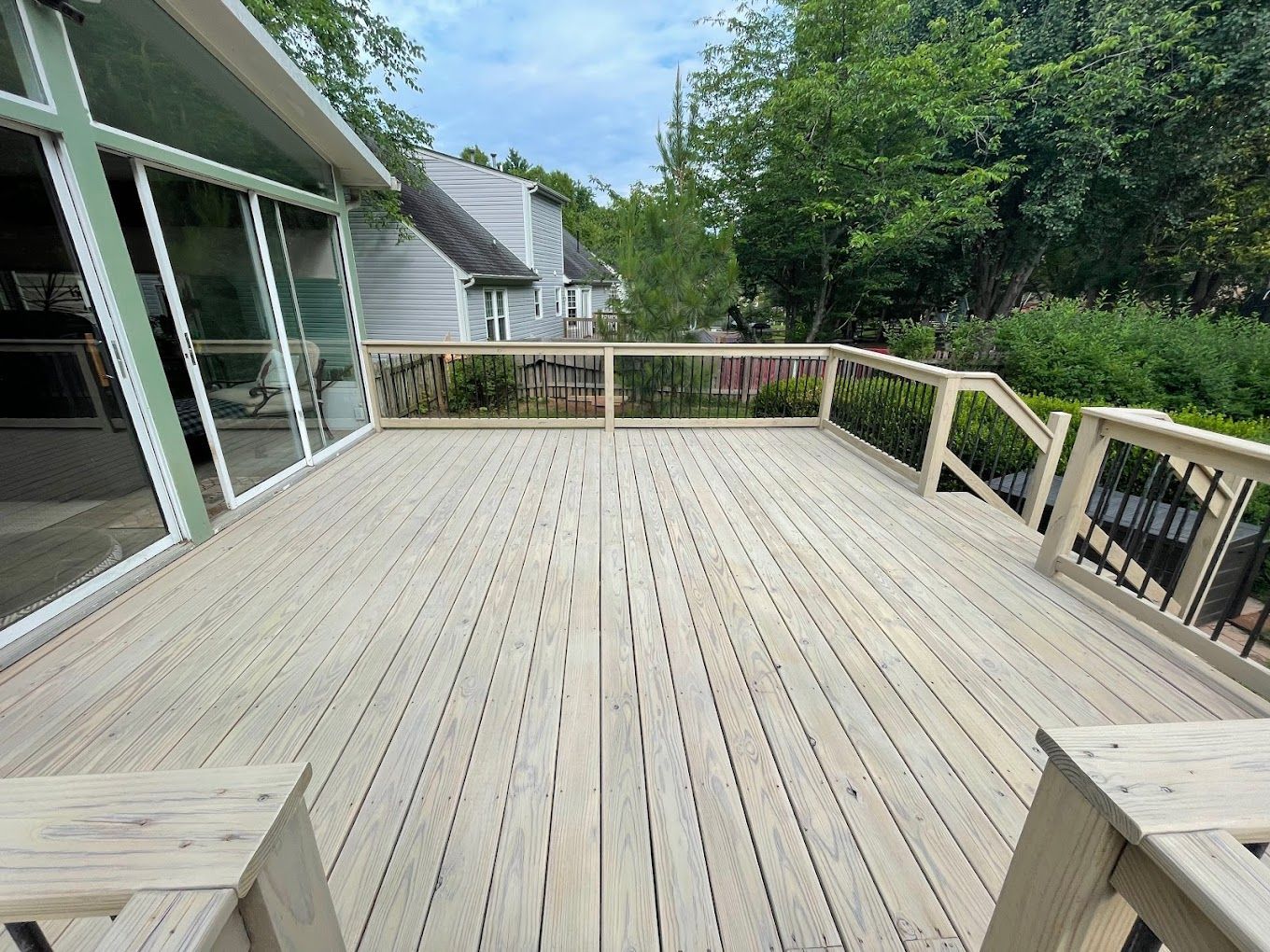 A large wooden deck with a railing and benches in front of a house.