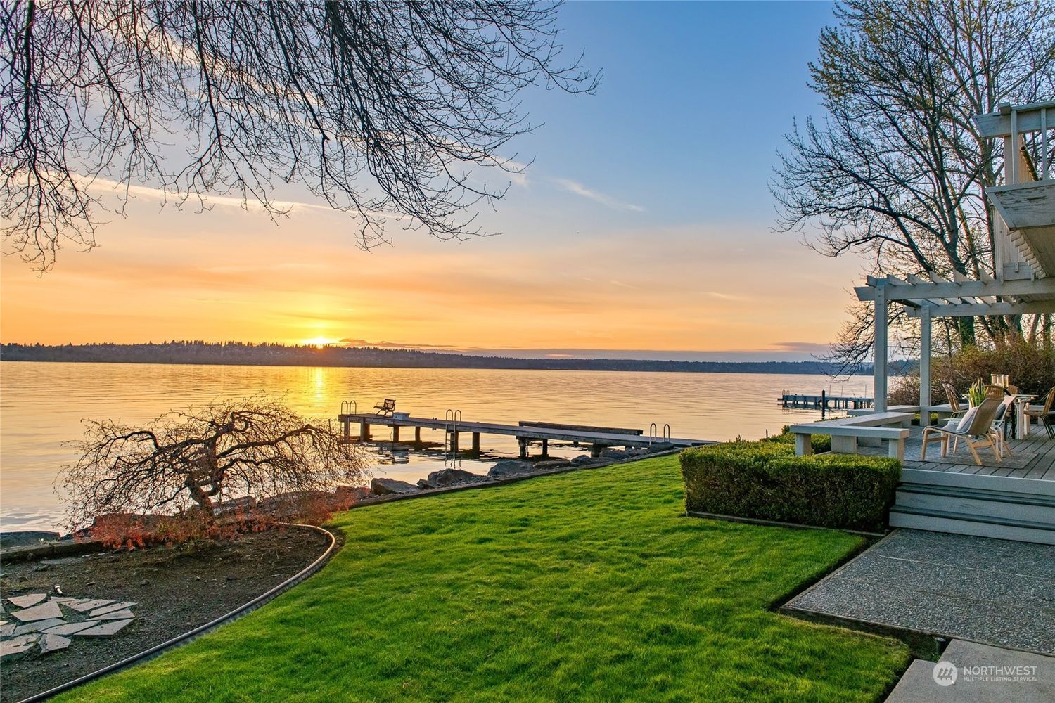 A sunset over a lake with a house in the foreground and a dock in the background.