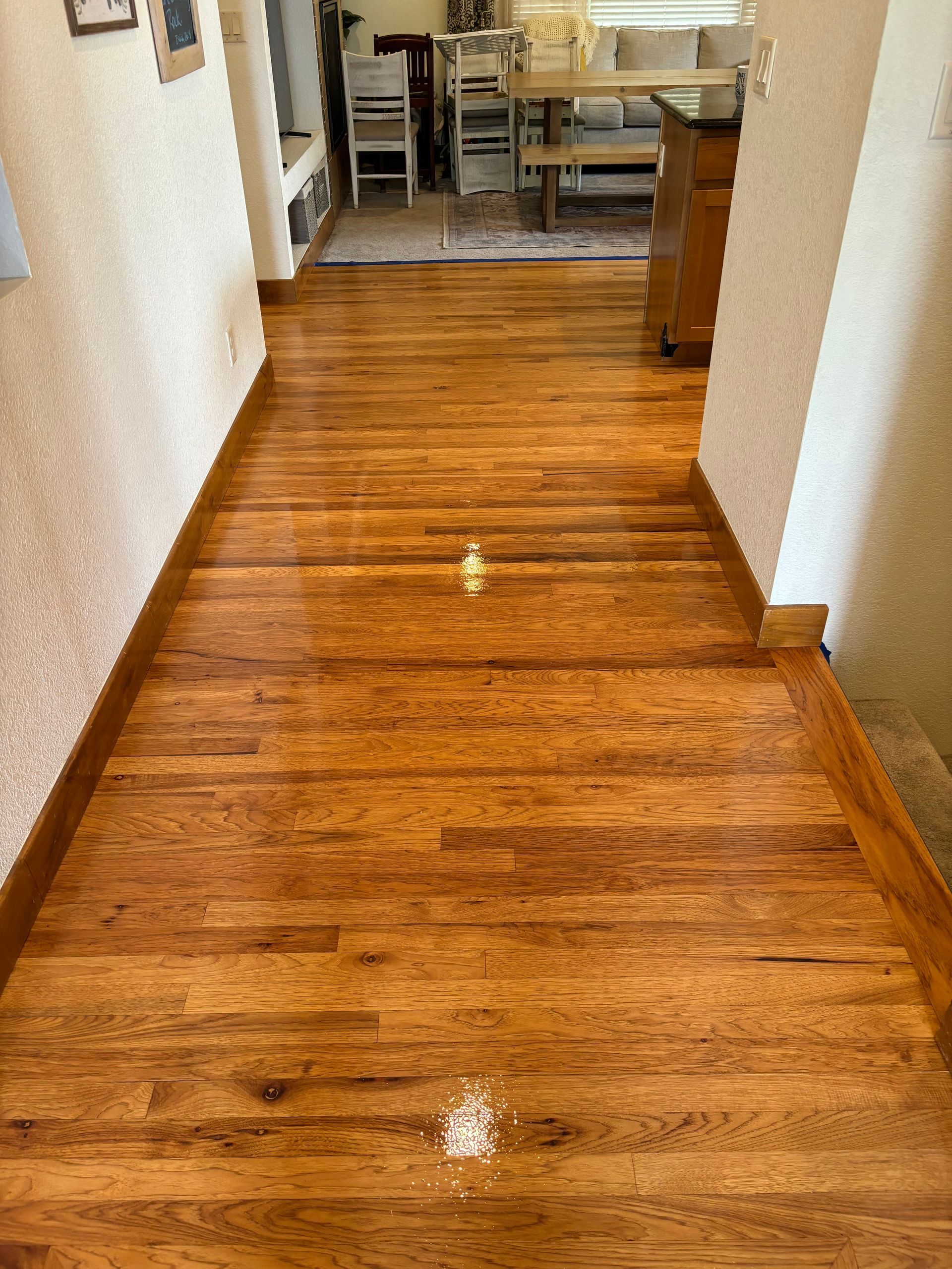 A hallway with a wooden floor and a dining room in the background.