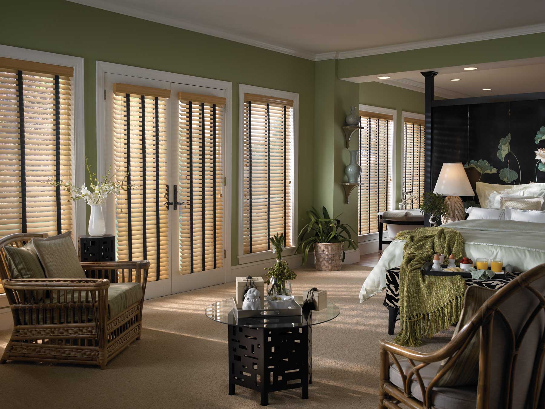 Bedroom with woven blinds, wicker furniture, green walls, and sunlight.