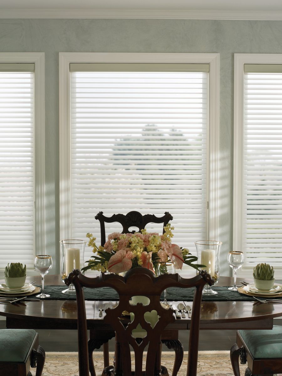 Dining room with table set for a meal, floral centerpiece, and window blinds.