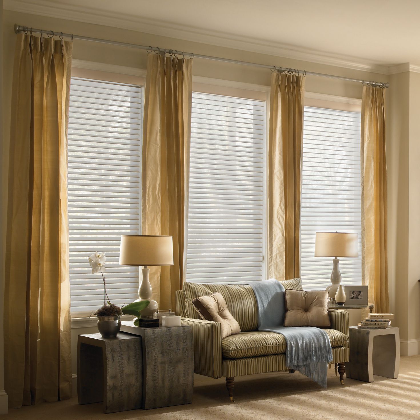 Living room with blinds, drapes, sofa, end tables, lamps. Neutral color palette: gold, brown, beige.