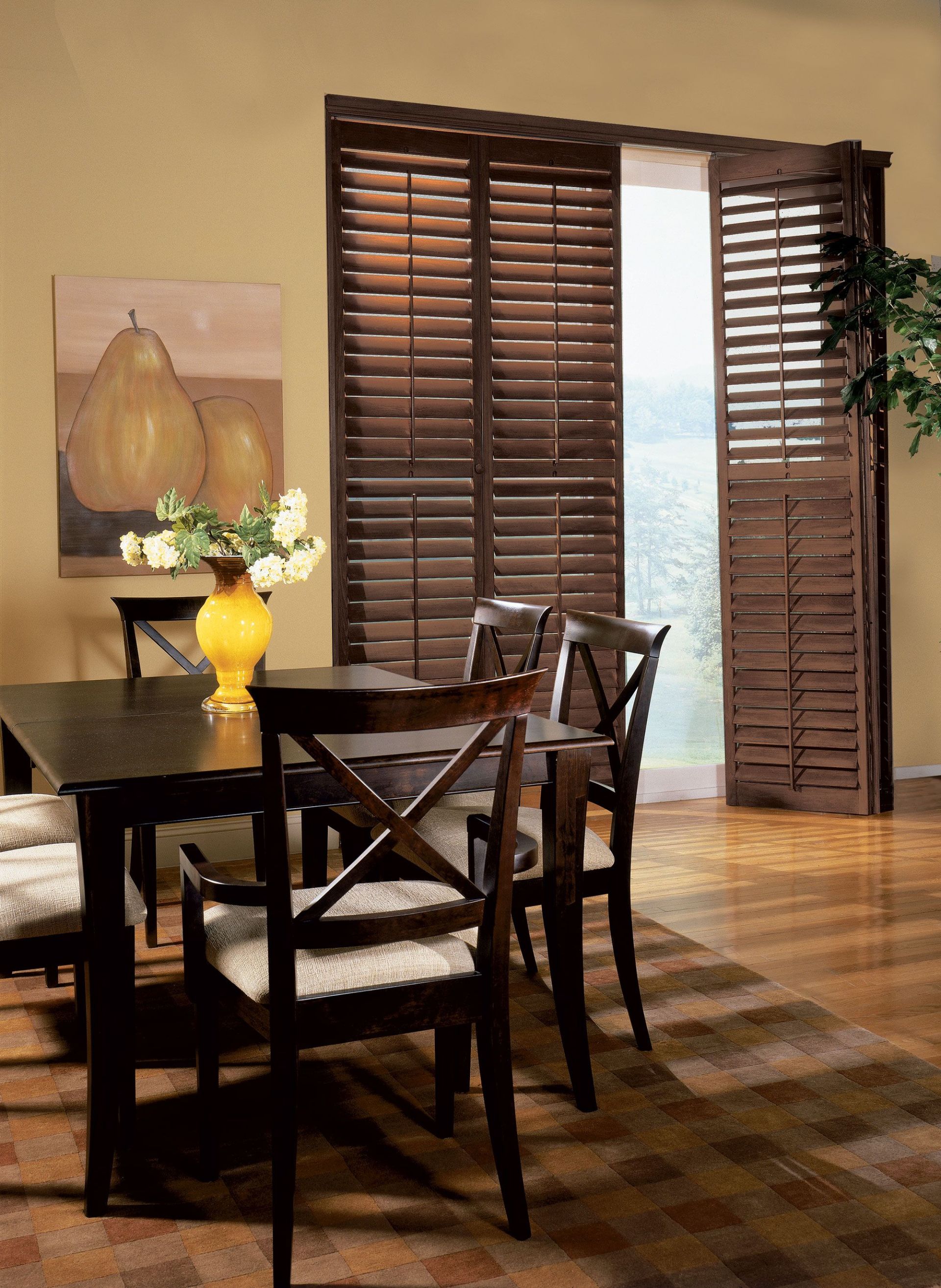 Dining room with a dark wooden table and chairs, a painting of pears, and a window with wooden shutters.