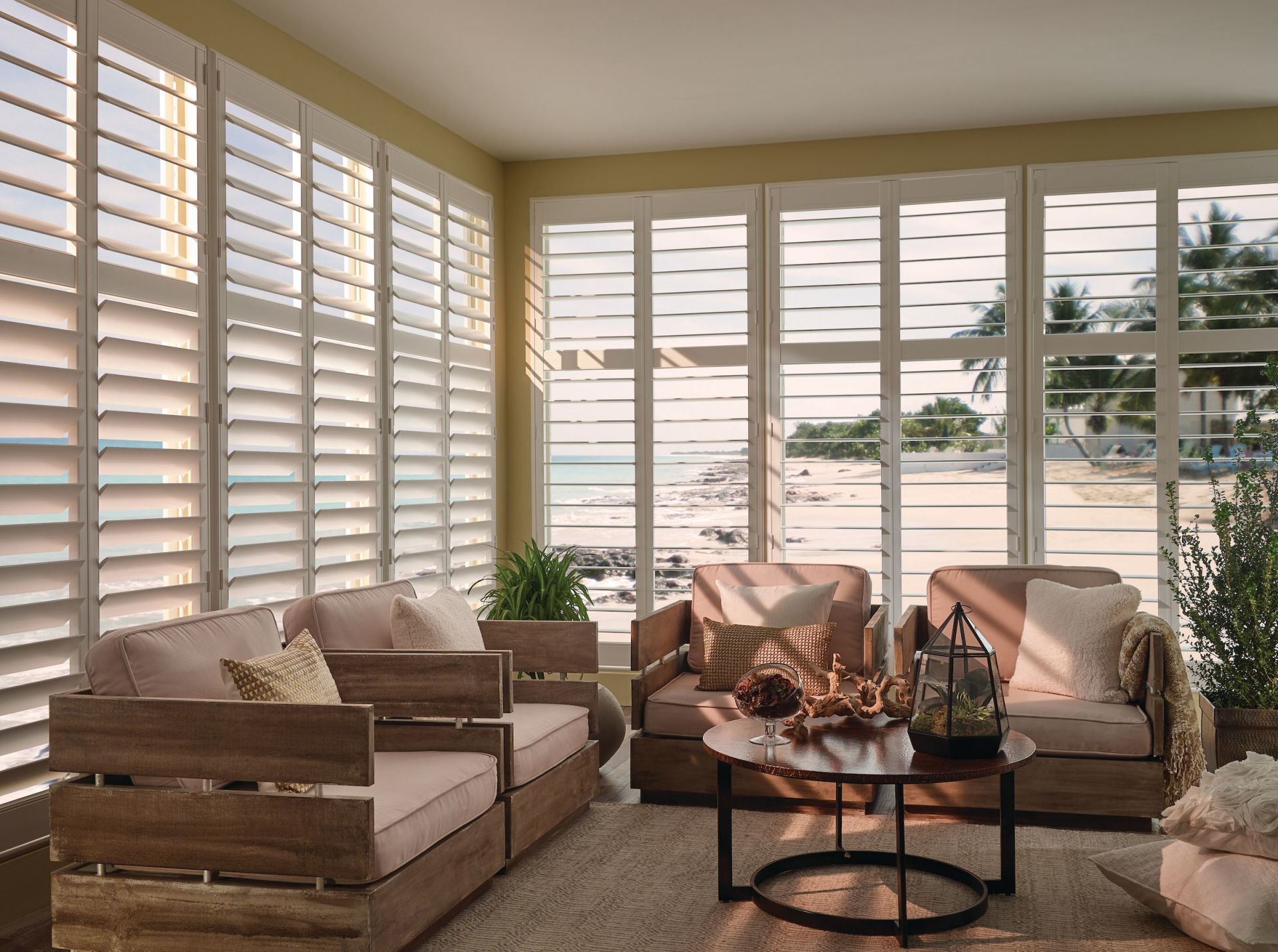 Living room with white shutters, beach view, wooden furniture, and decorative items.