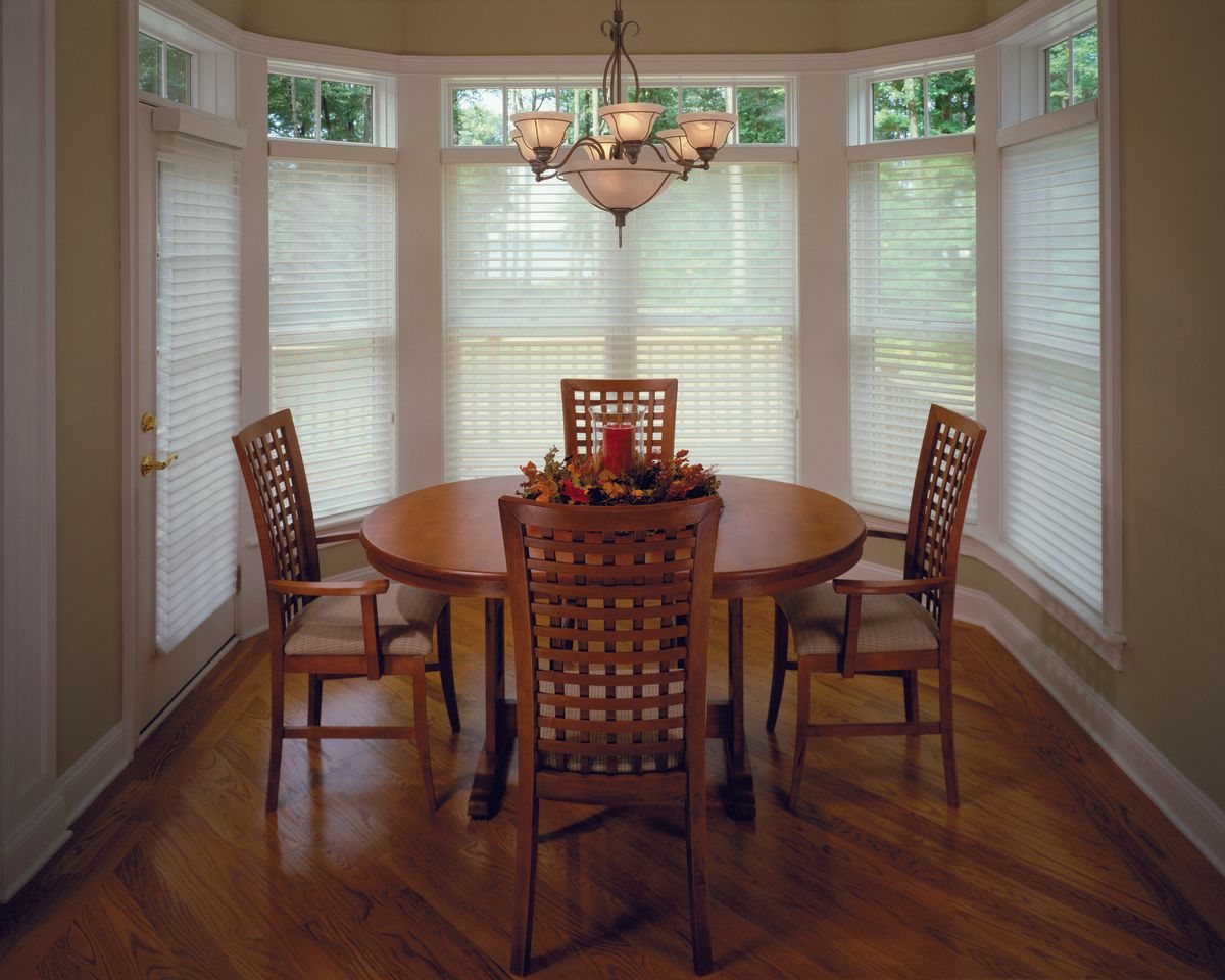 Dining area with round wooden table, four chairs, and bay window with blinds.
