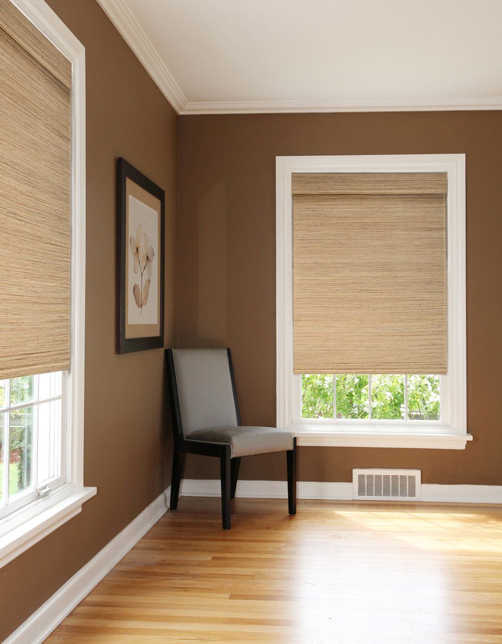 Room with brown walls, wooden floor, windows with woven blinds, and a chair.