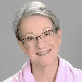 Woman with short gray hair and glasses smiles. Wearing a pink shirt.