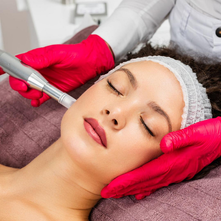 A woman is getting a facial treatment with red gloves on her hands.