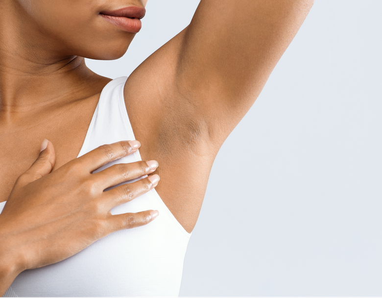 A woman in a white tank top is holding her armpit.