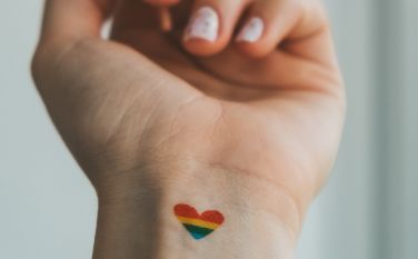 A person has a rainbow heart tattoo on their wrist.