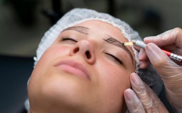A woman is getting her eyebrows tattooed with a machine.