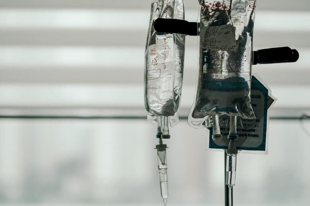 Two IV fluid bags hanging on poles in a hospital setting