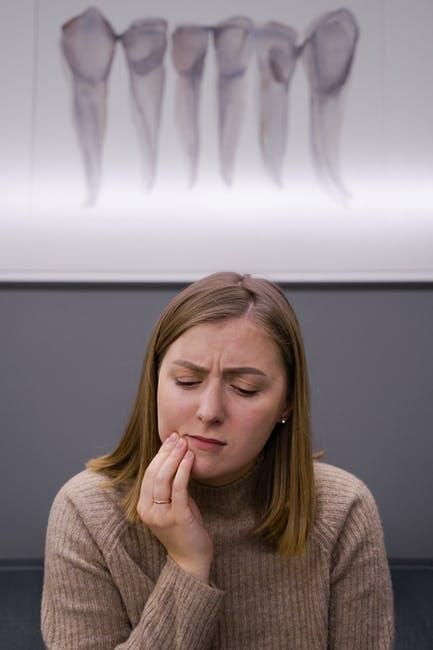 A person with a pained expression holding their jaw in front of a dental office wall graphic.