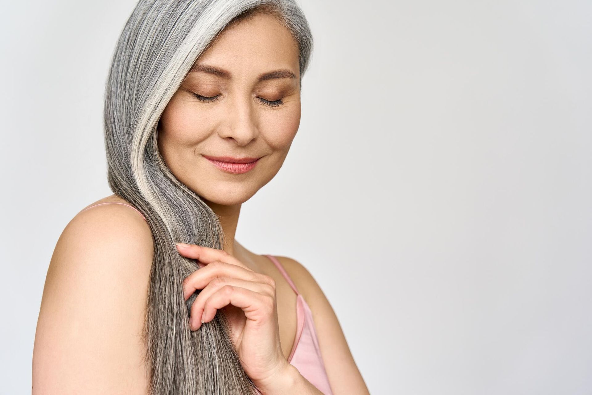 A woman with gray hair is smiling and touching her hair.