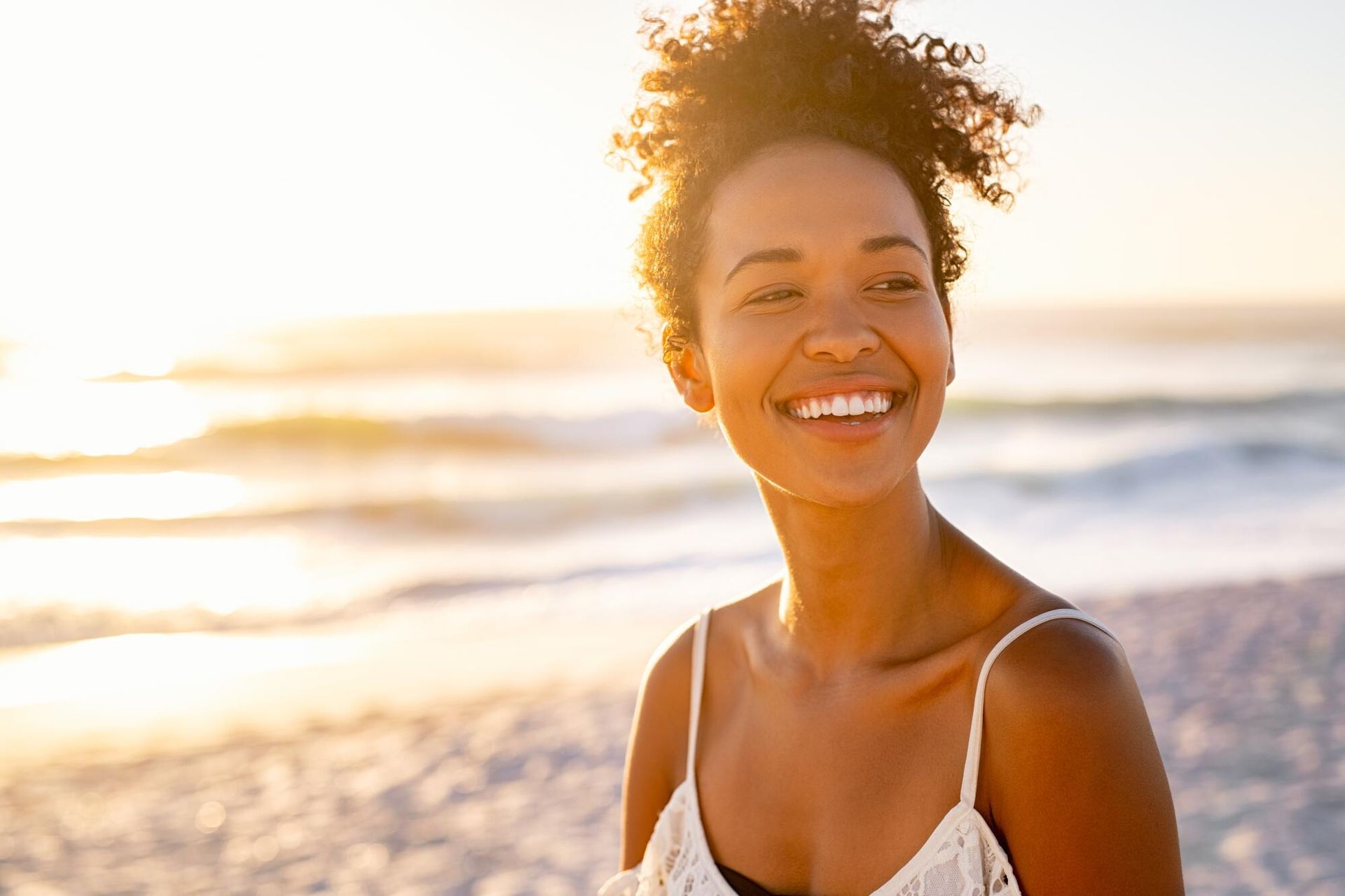 A woman is smiling on the beach at sunset.