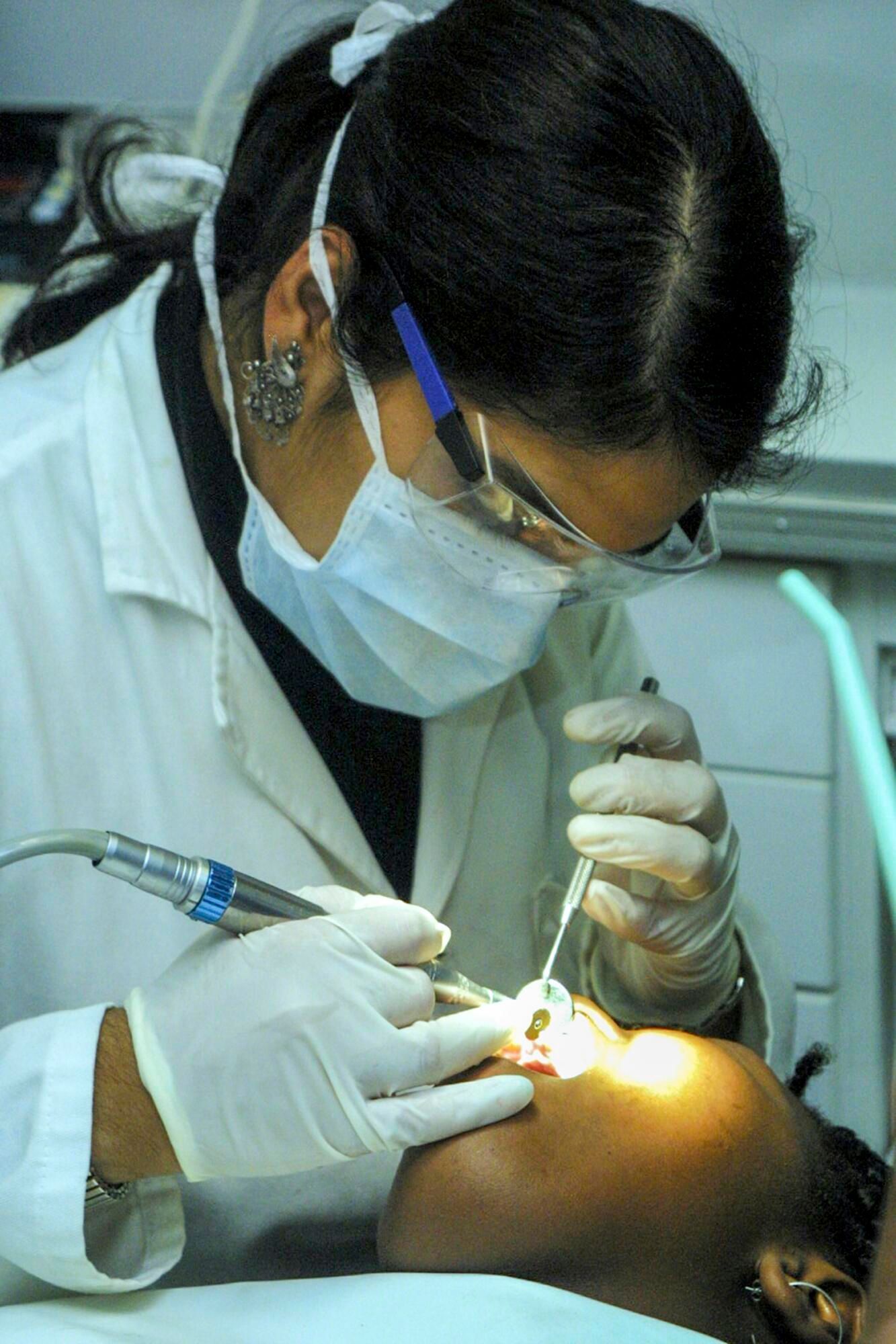 Dentist in a white coat working on a patient's mouth, using tools.
