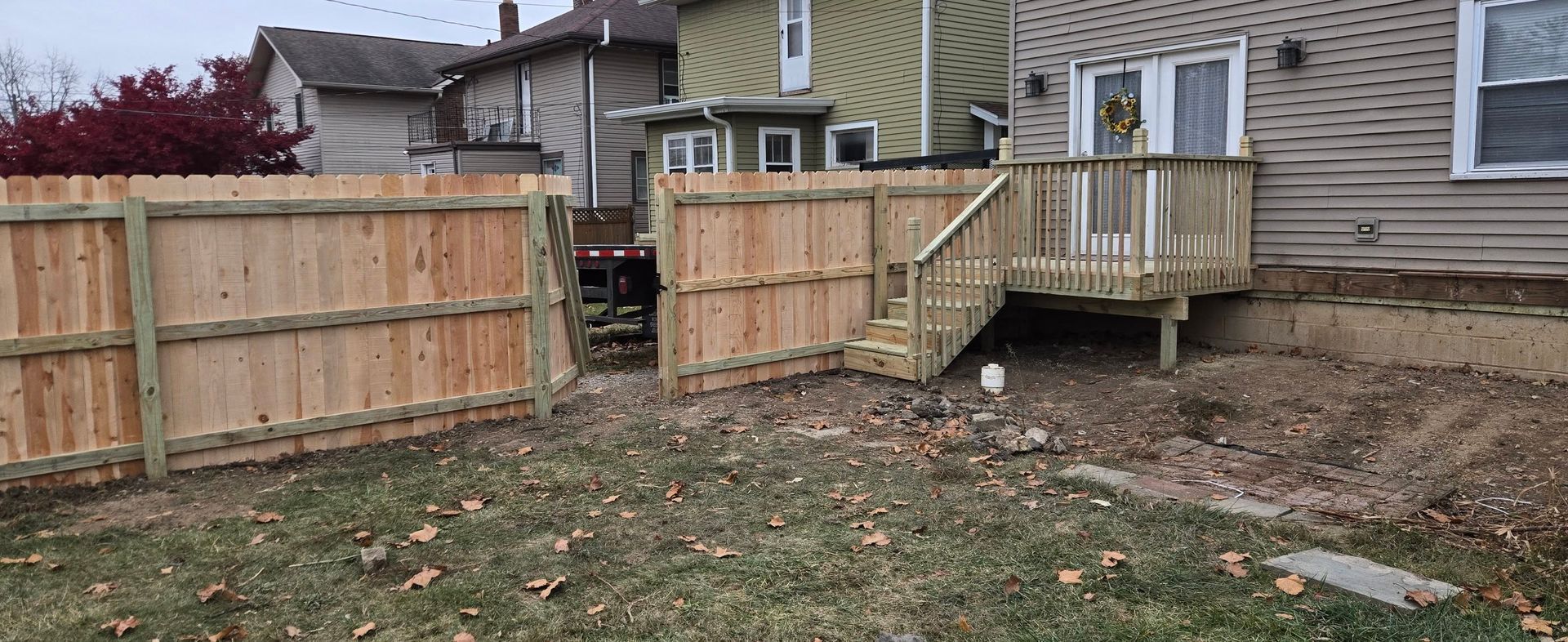 A wooden deck with stairs attached to a house exterior, next to a newly installed wooden privacy fence in a backyard.