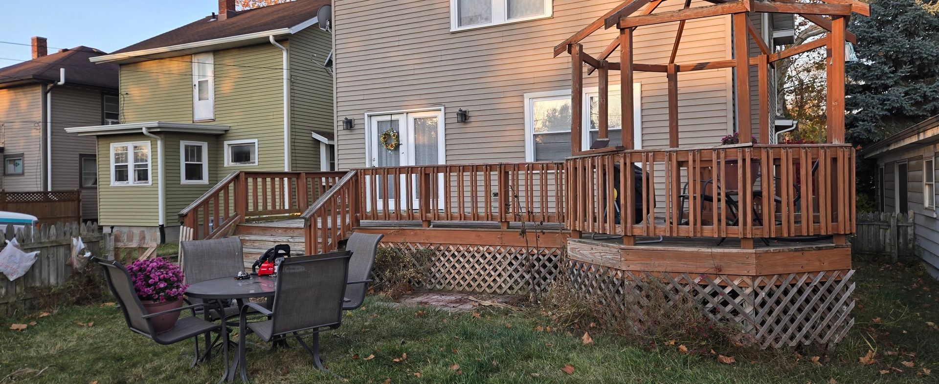 A wooden deck with a gazebo attached to the back of a house, featuring outdoor furniture on the lawn.