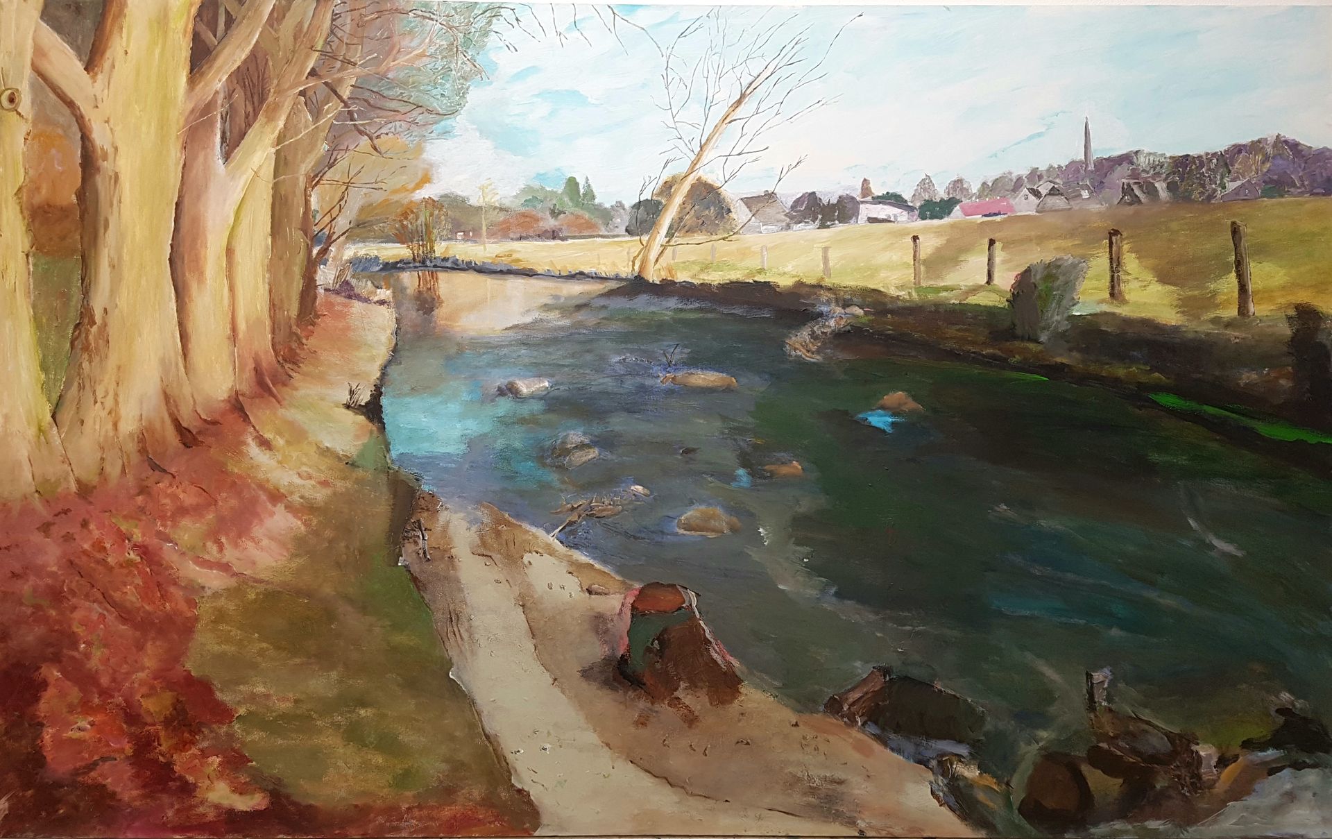Ein Flußlauf. Steine und Barrieren lassen die Strömung erkennen. Eine Baumreihe säumt das Ufer. Gegenüber der Blick auf das Dorf.