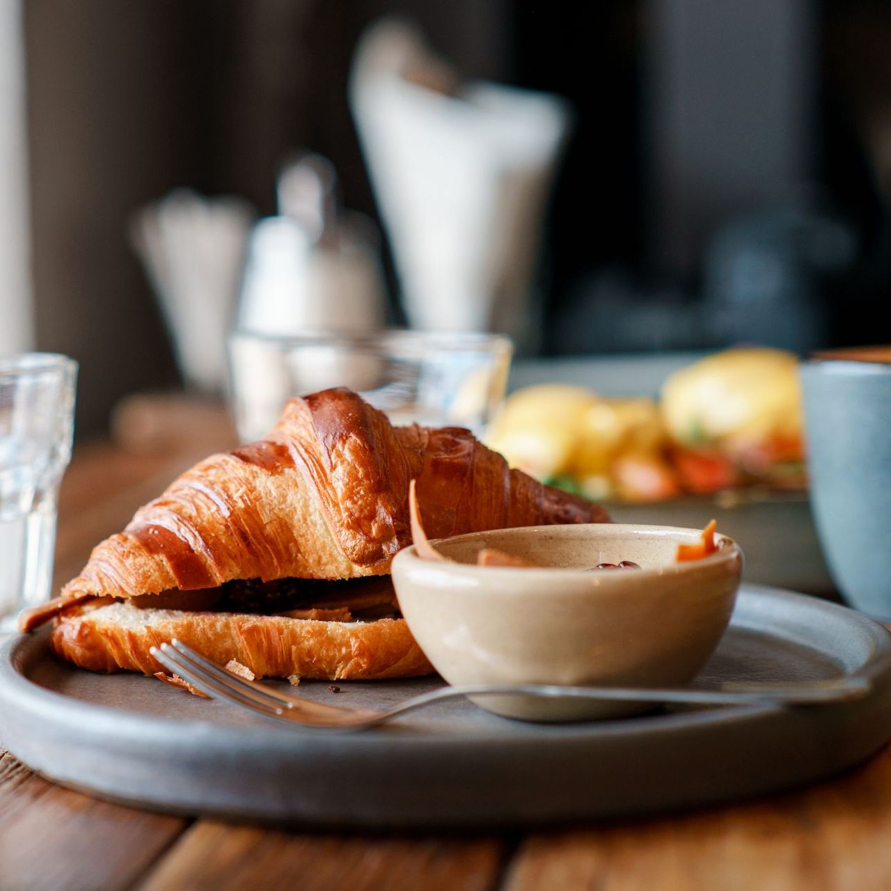 A croissant and a bowl of dipping sauce on a plate