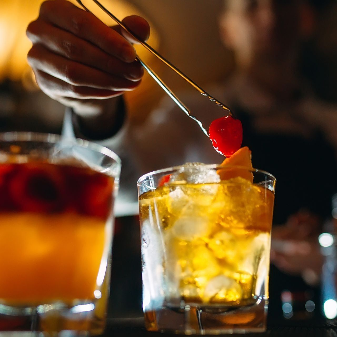 A person is adding a cherry to a drink with tongs