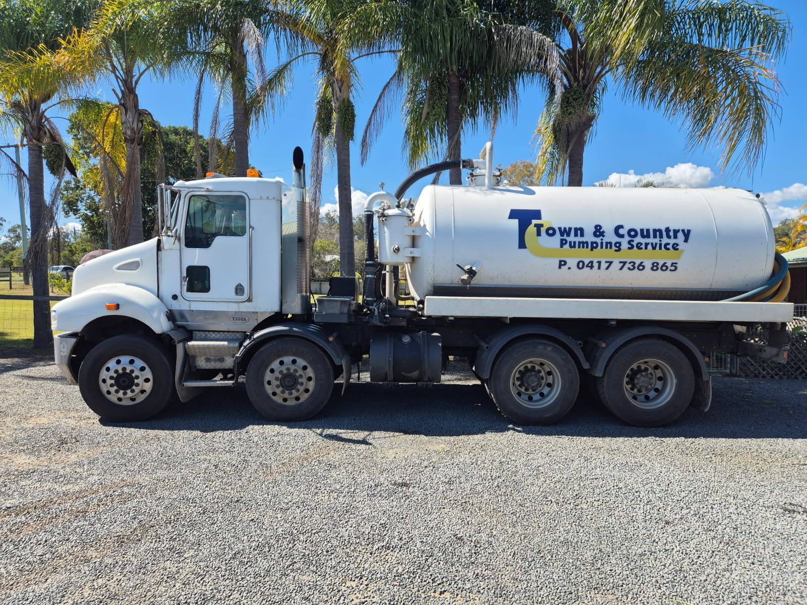 Orange septic tank truck parked on grassy driveway, hose extended.
