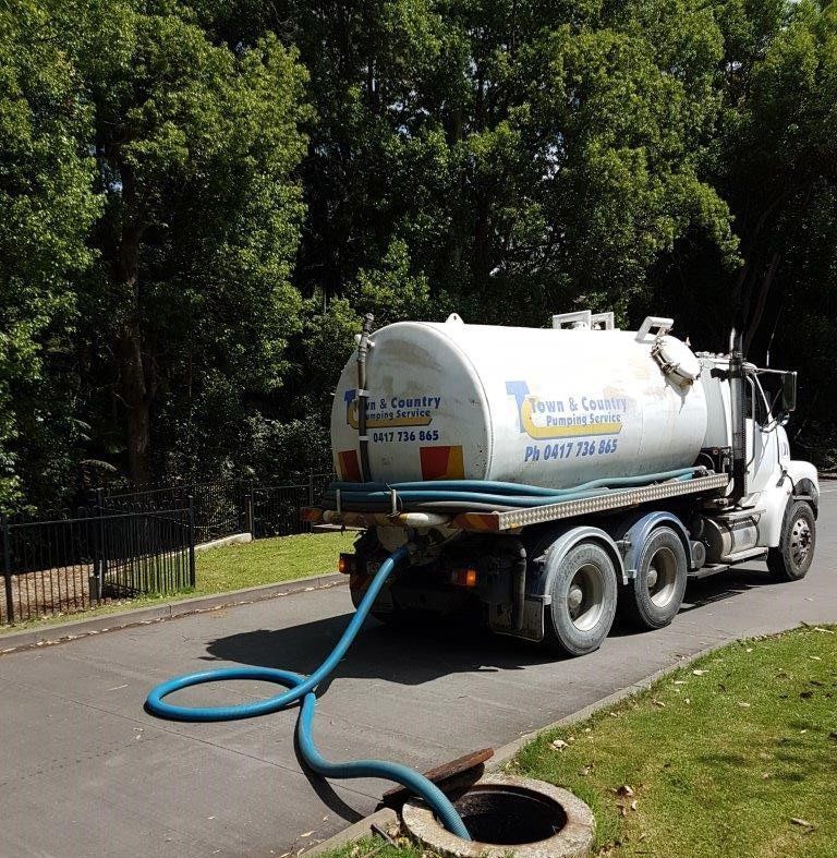A red hose connected to a white tank truck, extending onto a paved surface.