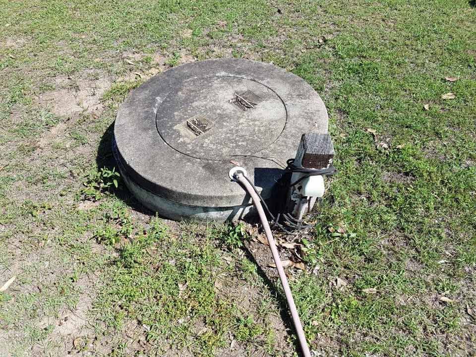 A person vacuuming a septic tank with a large hose, in a dirt setting.
