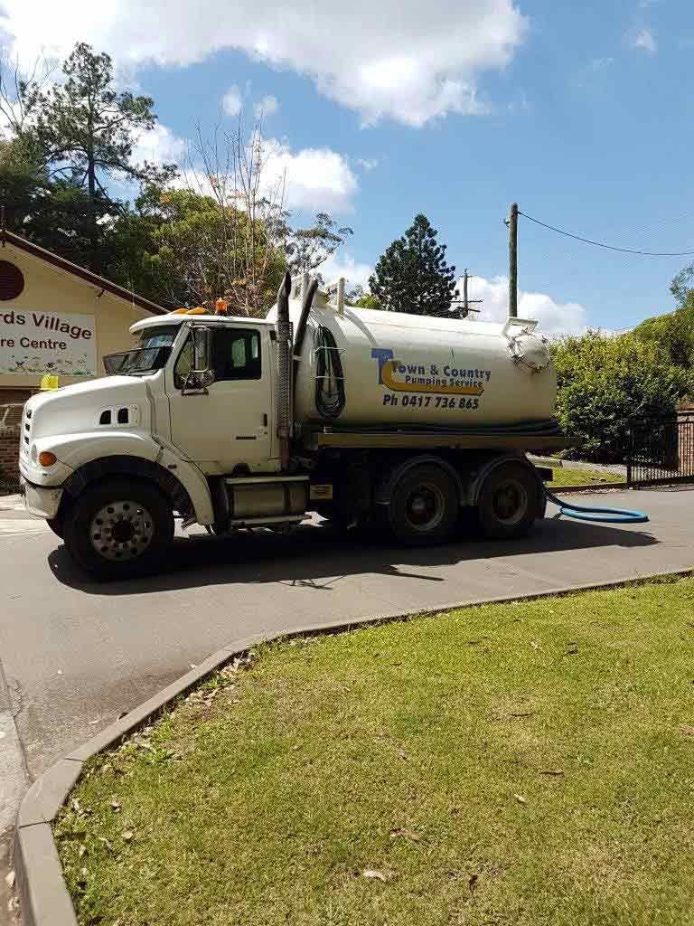 Construction worker near open manhole; orange safety vest, blue jeans, asphalt pavement, and equipment visible.