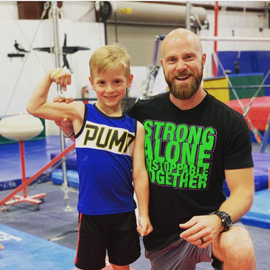 A man and a boy are posing for a picture and the boy is wearing a shirt that says strong alone
