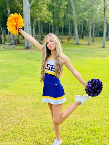 A woman with curly hair is smiling with her arms in a cheer pose. 