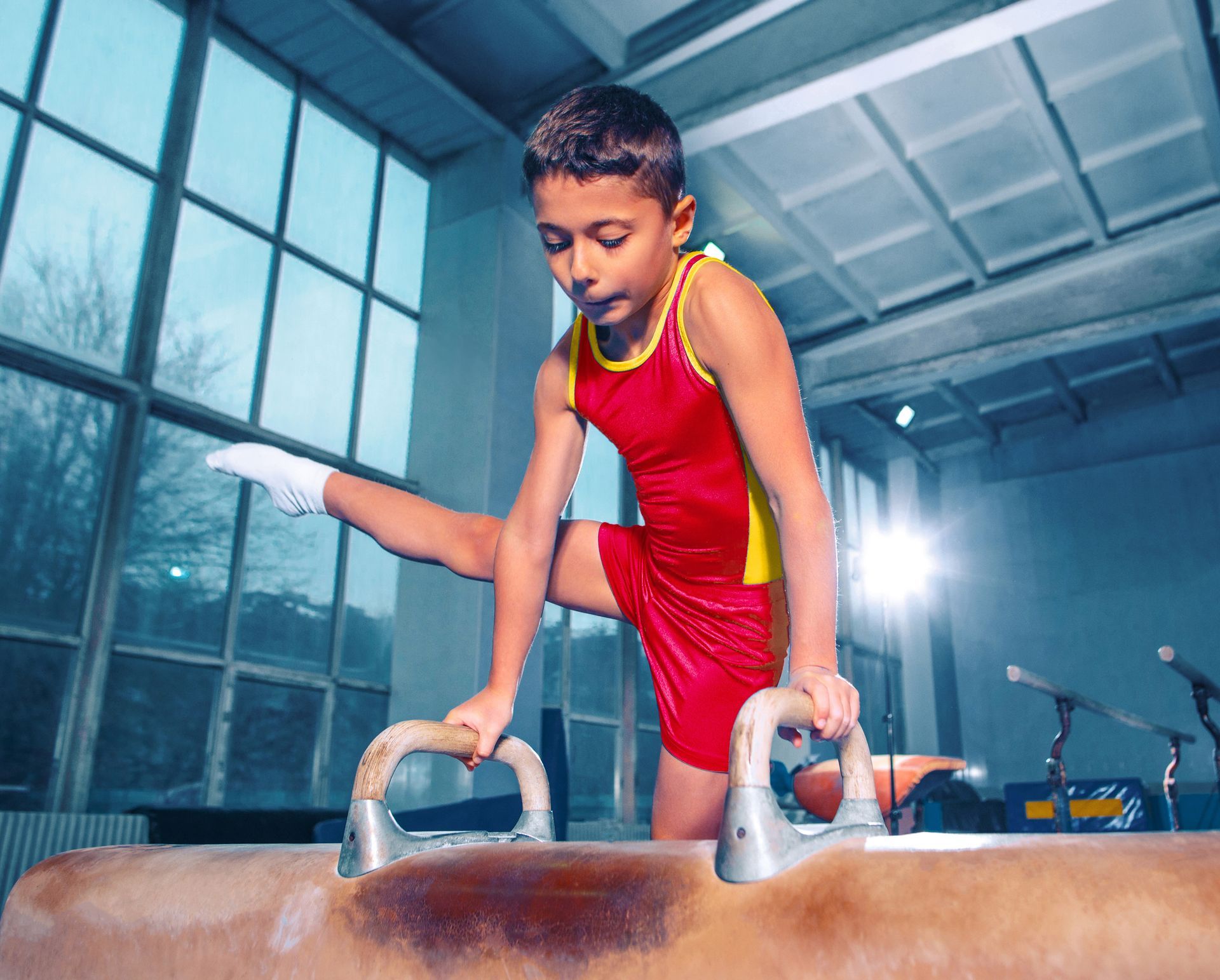 A young boy is doing a trick on a pommel horse in a gym.