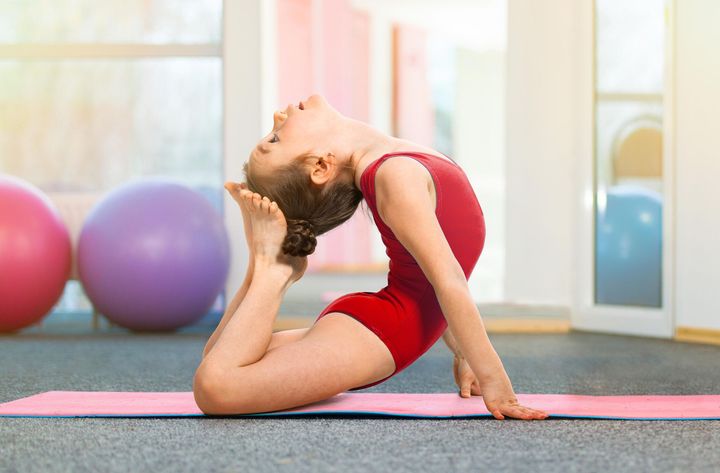 A young girl is doing a yoga pose on a yoga mat in a gym.