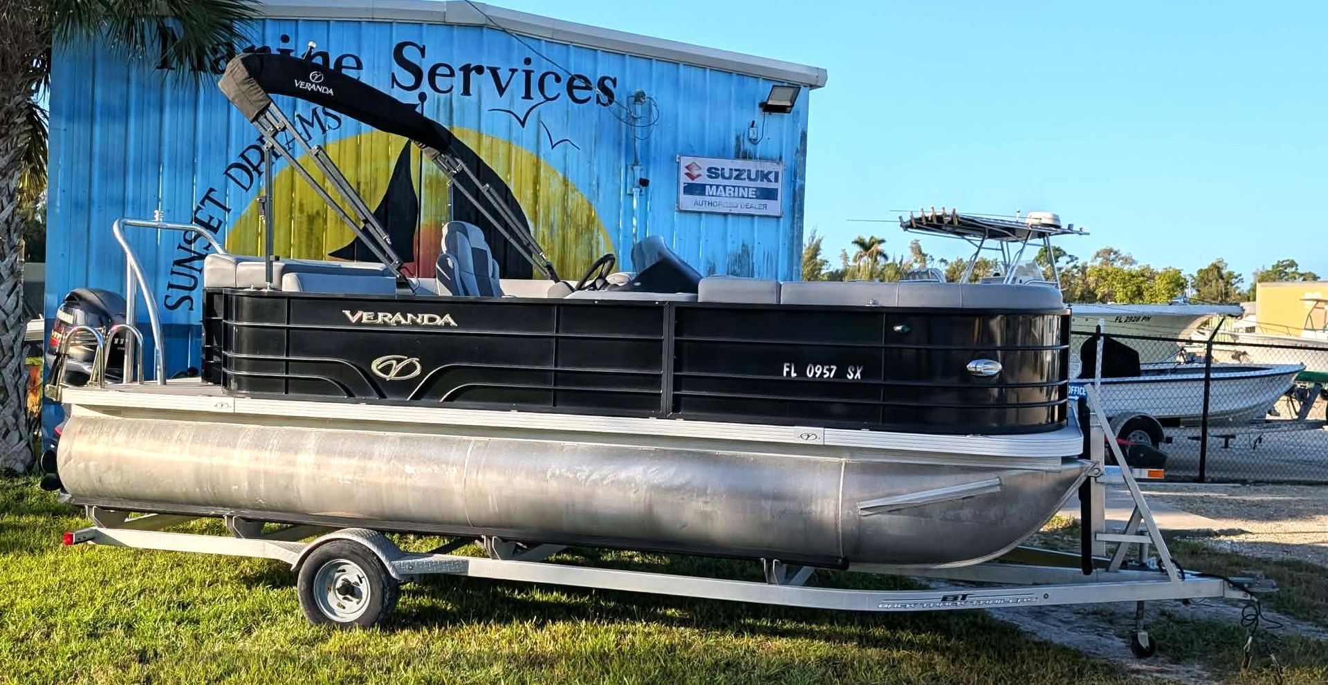 Black pontoon boat on a trailer in front of a blue service shop sign