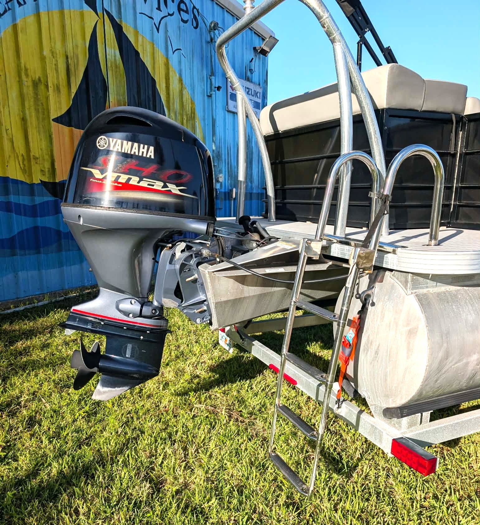 Yamaha outboard motor attached to a small aluminum boat trailer on grass beside a blue wall
