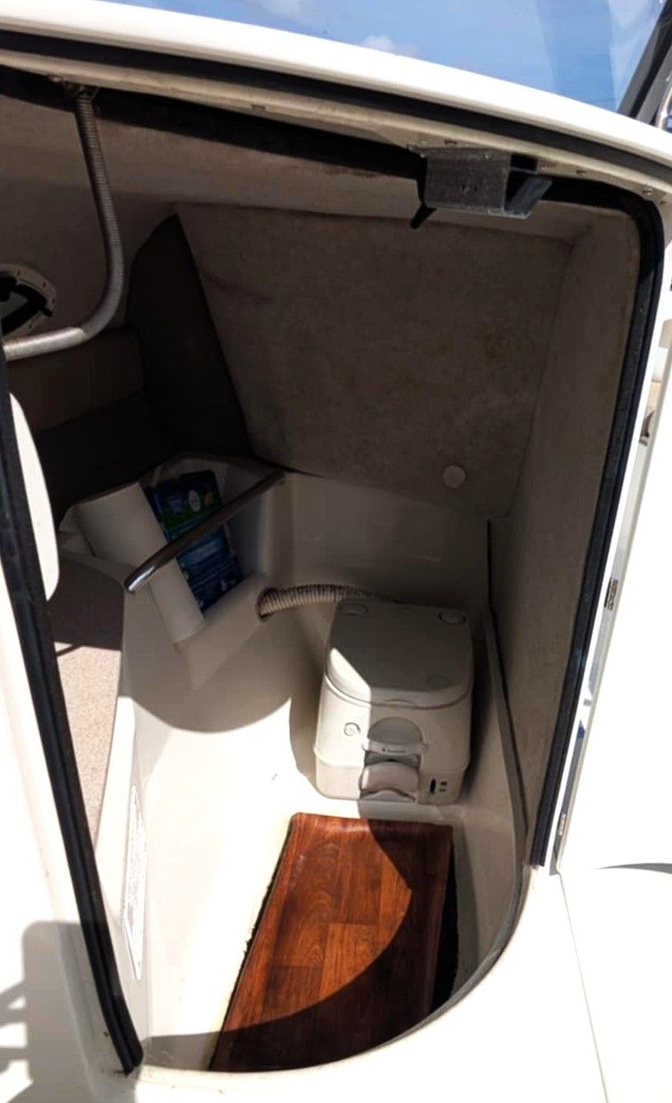 Compact boat cabin with beige seating, storage, and a wood floor visible through an open doorway