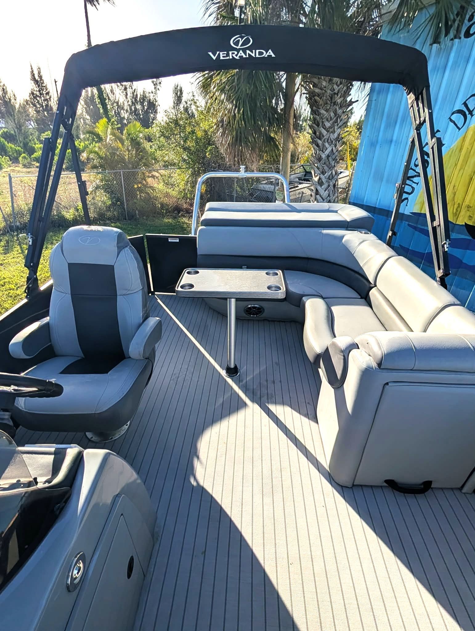 Boat deck with gray seating, canopy, and tables on a calm waterway surrounded by trees.