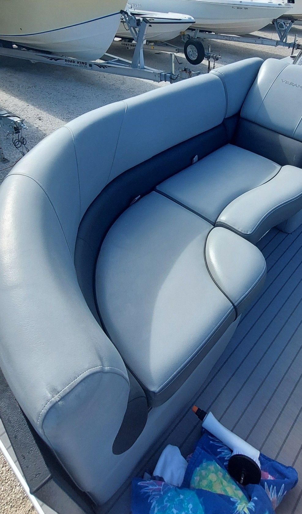Gray curved boat bench seat on a deck, with blue floorboards and part of the boat visible above.