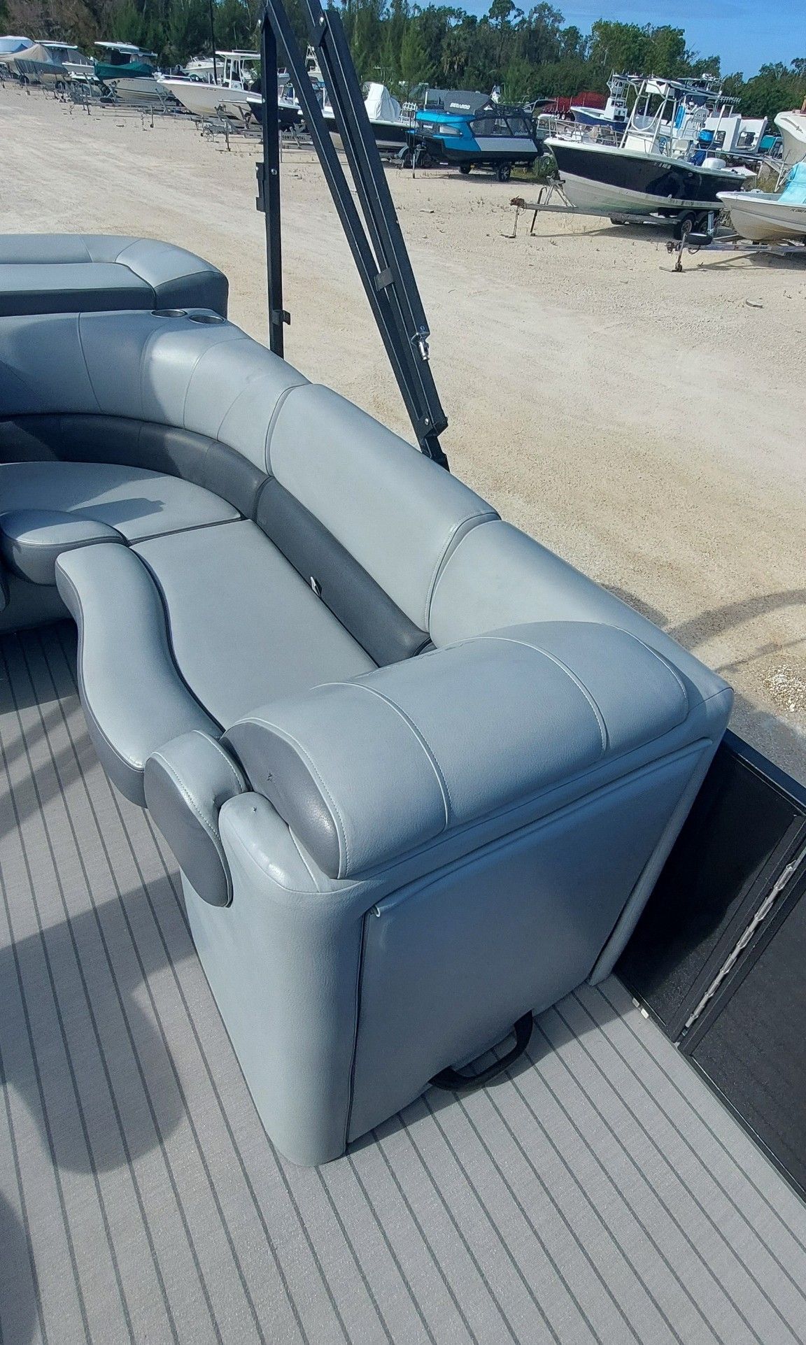 Gray cushioned pontoon boat bench seat on a deck at a marina, with boats in the background