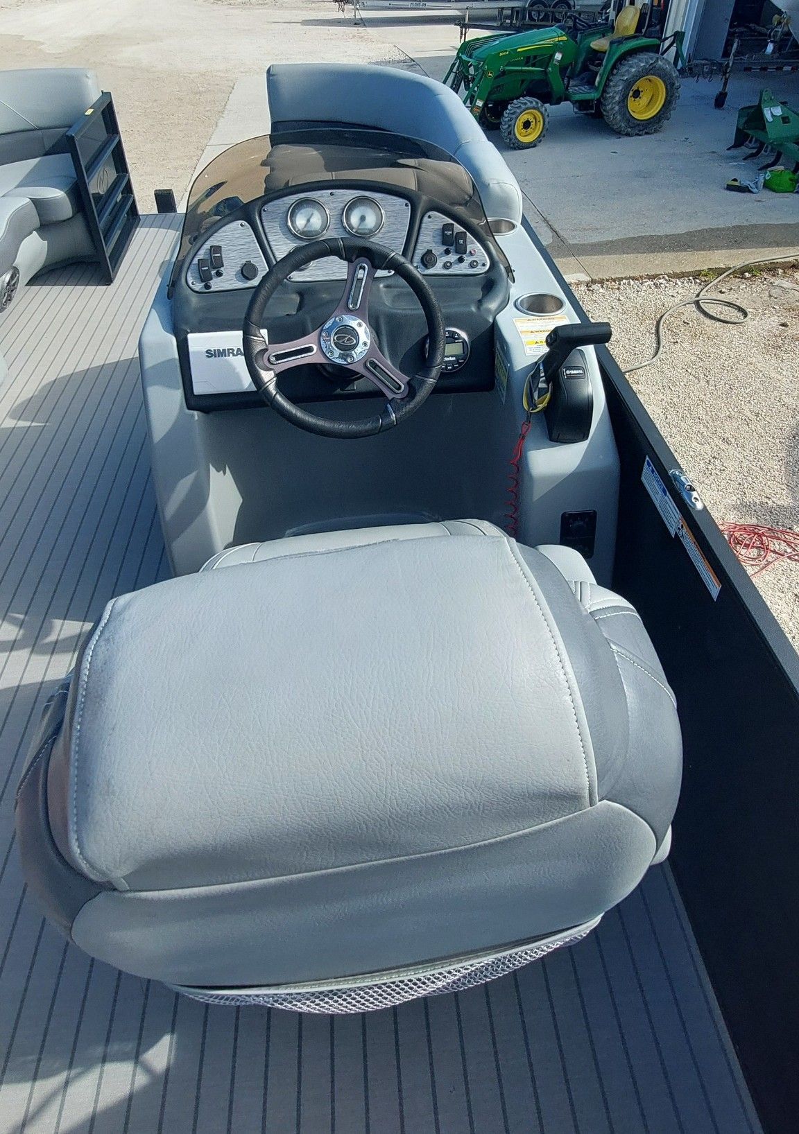 Gray boat seat and steering console on a dock, with a green tractor in the background.