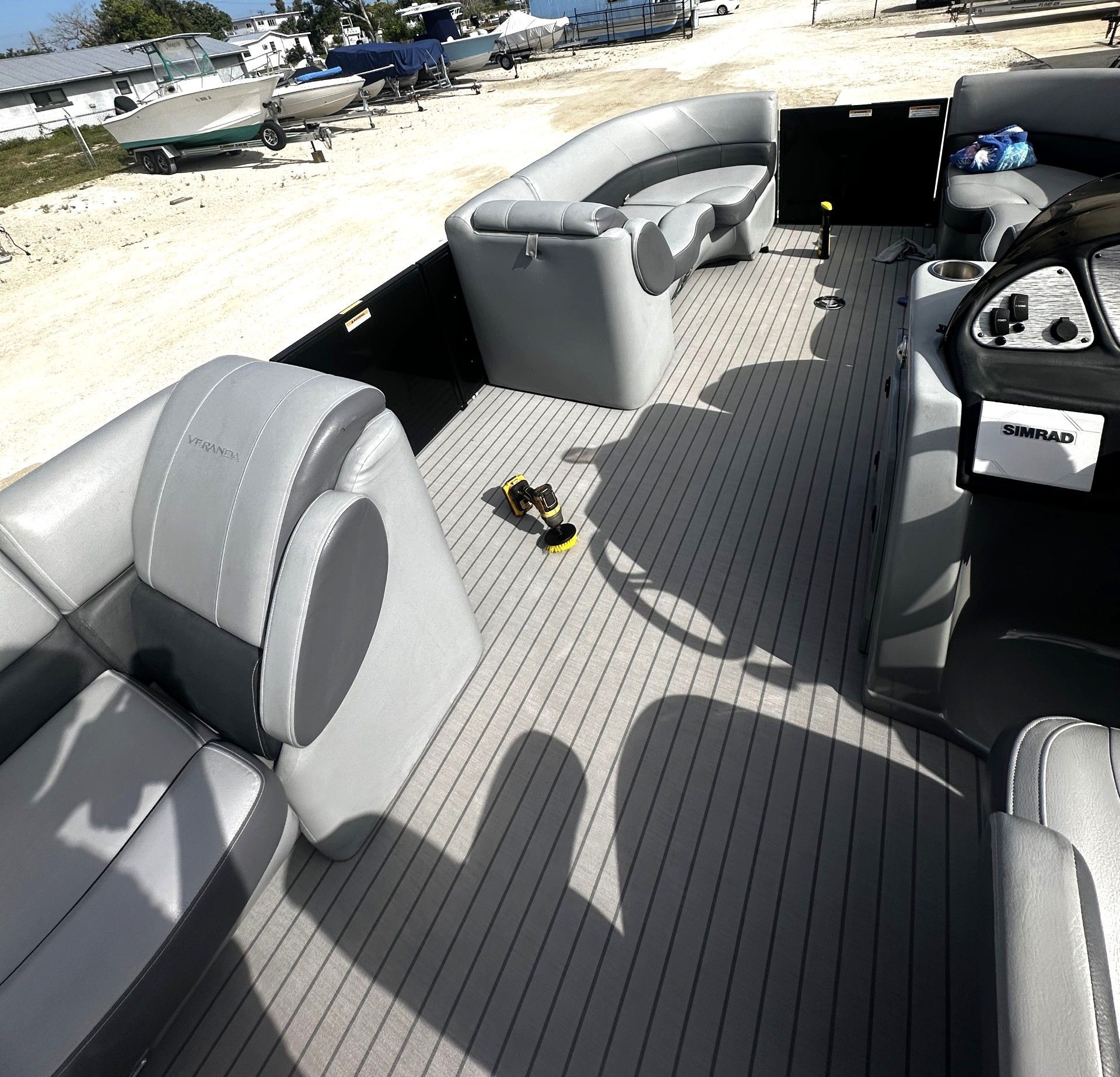 Gray pontoon boat deck with seats on a sandy beach, viewed from the interior.