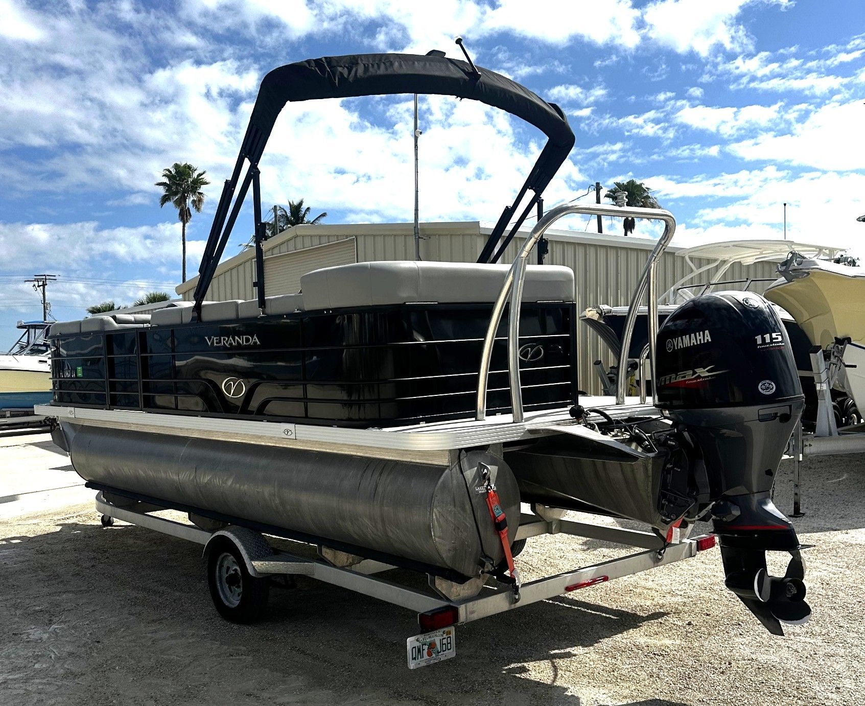 Pontoon boat on a trailer at a marina, with a black Bimini top and outboard motor
