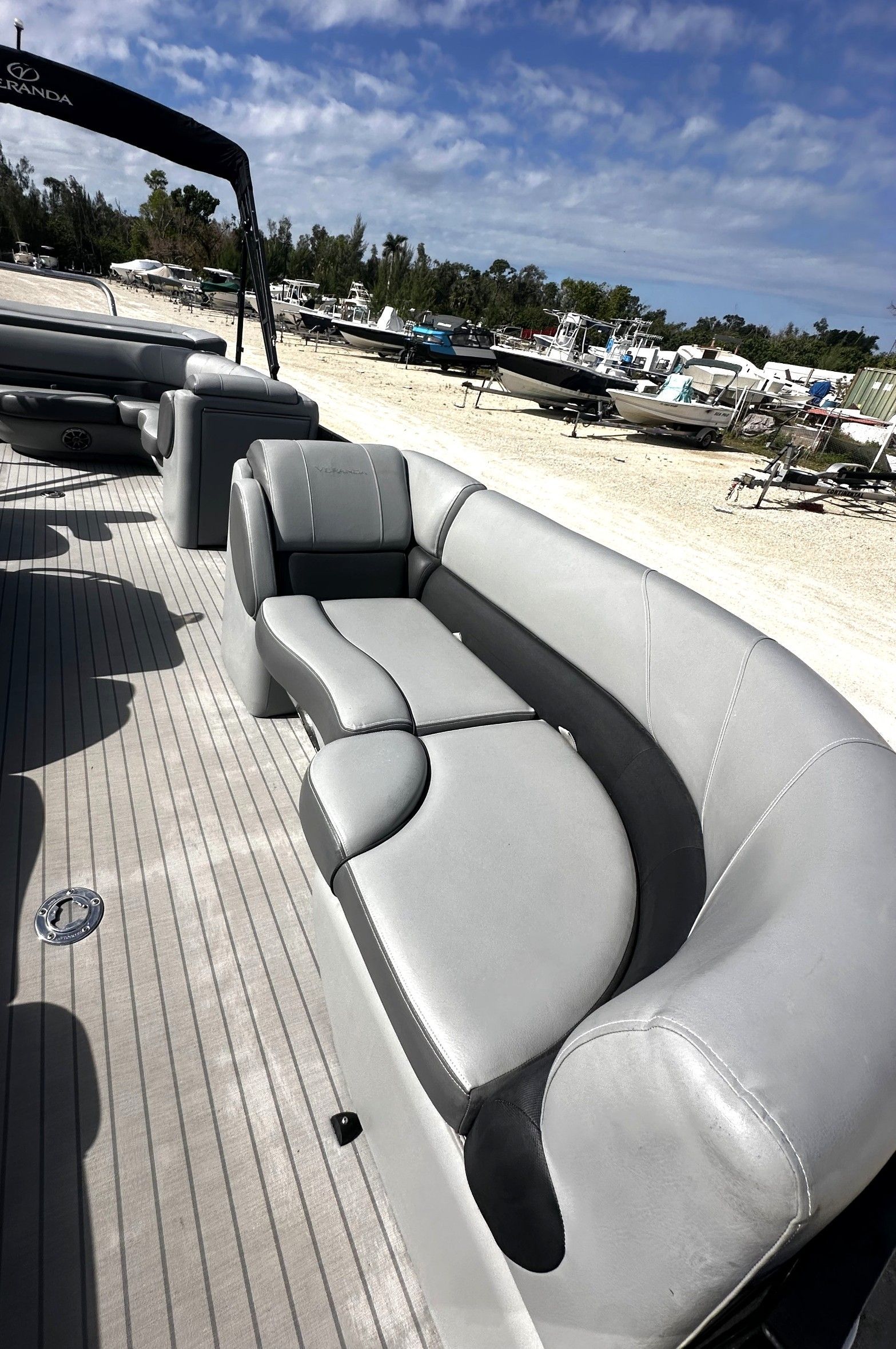 Curved gray boat seating on a sunny sandy beach with blue sky and palm trees in the background